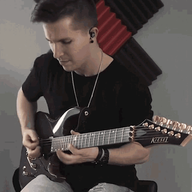 a man playing a kiesel electric guitar in front of a wall