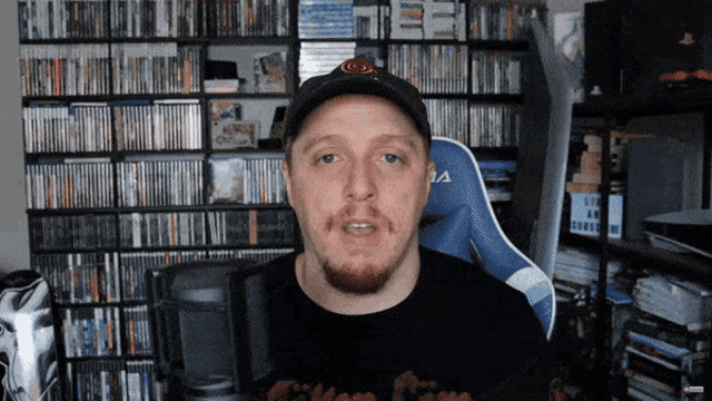 a man wearing a black hat and a black shirt with the letter a on it is talking into a microphone