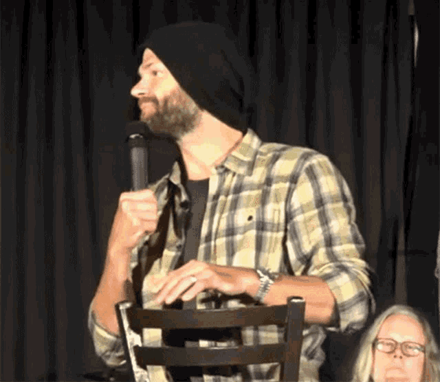 a man in a plaid shirt is holding a microphone while sitting on a chair