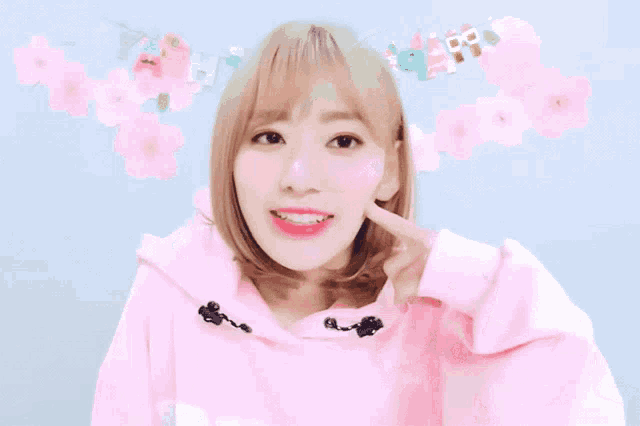 a girl wearing a pink hoodie is smiling and pointing to her face