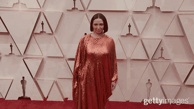 a woman in a red dress stands in front of a wall with oscar statues on it