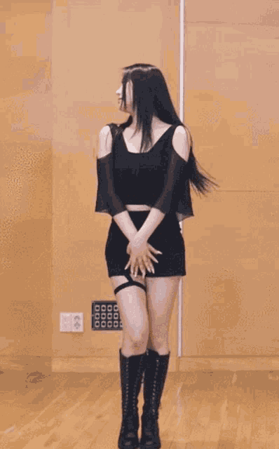 a woman in a black crop top and black shorts is dancing in a room .