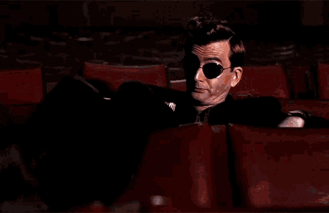 a man is sitting in a theater eating popcorn while watching a movie .