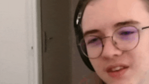 a young man wearing headphones and glasses is looking at the camera .