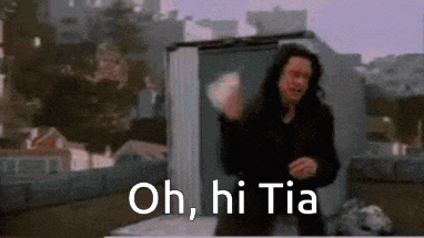 a man with long hair is standing on a roof with the words oh , hi tia written on it .