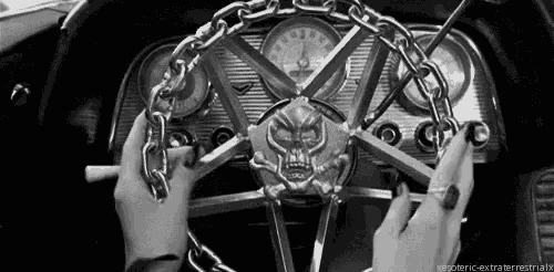 a black and white photo of a woman holding a steering wheel with chains around it