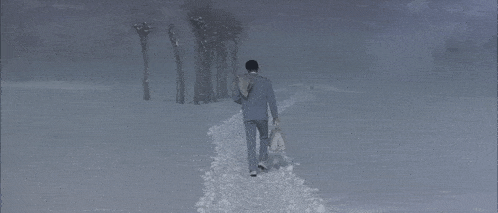 a man in a suit walks down a snow covered path