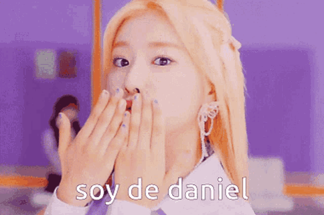 a woman with blonde hair is covering her mouth with her hands and the words soy de daniel written below her