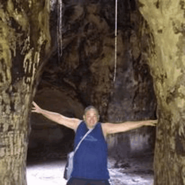 a man in a blue tank top is standing in a cave .
