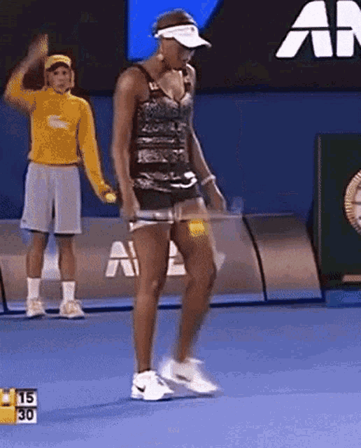 a woman is playing tennis on a court with a man in a yellow lacoste sweatshirt standing behind her