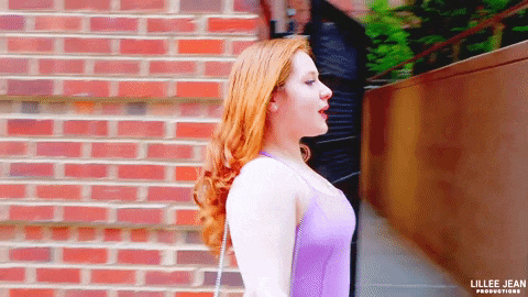 a woman in a purple dress is standing in front of a brick wall with the name lillee jean productions on the bottom