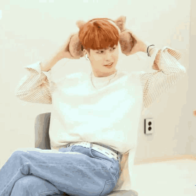 a young man with red hair is sitting in a chair with his hands behind his ears