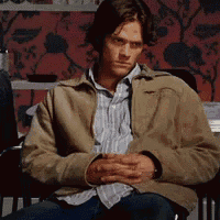 a man wearing a tan jacket is sitting in a chair with his hands folded