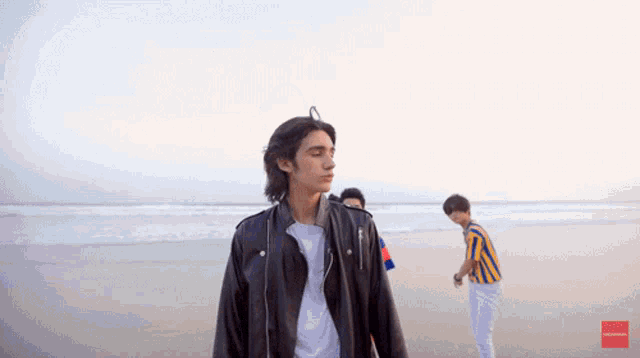 a man in a leather jacket stands on the beach