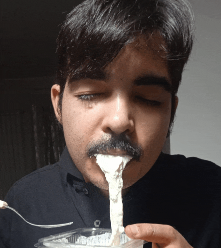 a man with a mustache is eating something with a spoon in his mouth