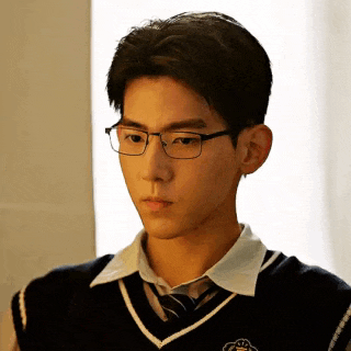 a young man wearing glasses and a vest and tie is looking down .