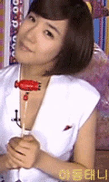 a woman in a white tank top is holding a red object in her hand with the letters ao on the bottom right