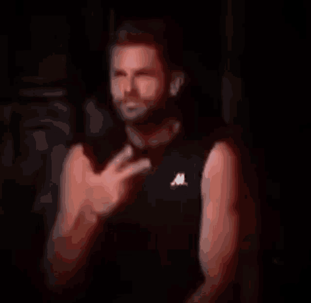 a man in a black sleeveless shirt is standing in the dark .