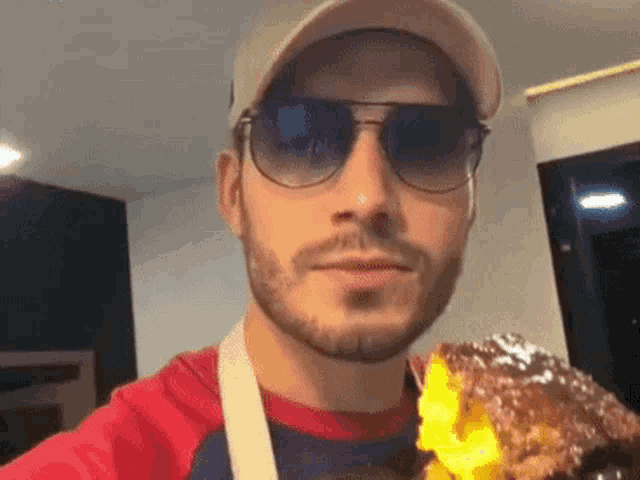 a man wearing sunglasses and a hat is holding a piece of chocolate cake .