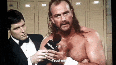 a shirtless wrestler is being interviewed by a man in a tuxedo while holding a microphone .