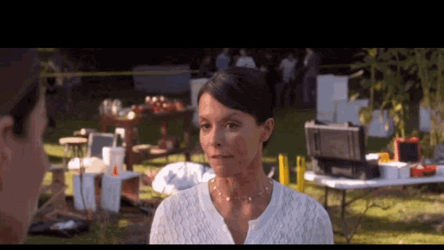 a woman in a white sweater talks to another woman in a field
