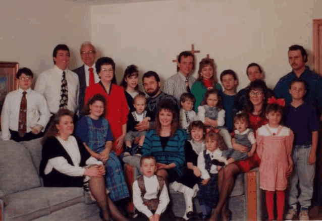 a large family posing for a picture with a cross on the wall behind them