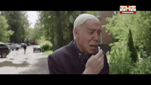 an older man smoking a cigarette in front of a sign that says thtg