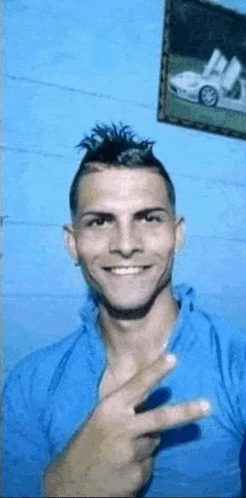 a man in a blue shirt is giving a peace sign .