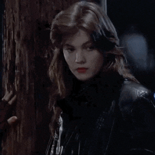 a woman in a black leather jacket is standing next to a tree trunk .