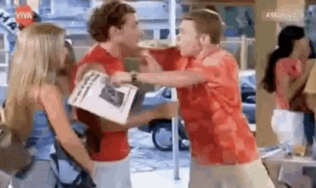 a man in a red shirt is holding a newspaper and a woman in a blue shirt is standing behind him .