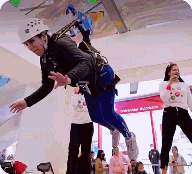 a woman wearing a helmet is flying through the air in front of a sign that says distribuidor autorizado