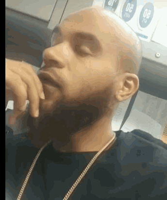 a bald man with a beard wearing a black shirt and a gold chain
