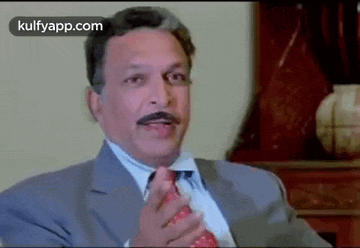 a man in a suit and tie is sitting in a chair and talking to someone .