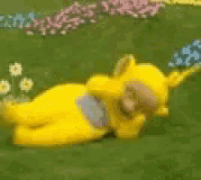 a yellow teddy bear is laying down in the grass .