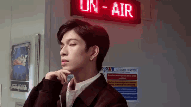 a young man is standing in front of a red sign that says `` on-air '' .