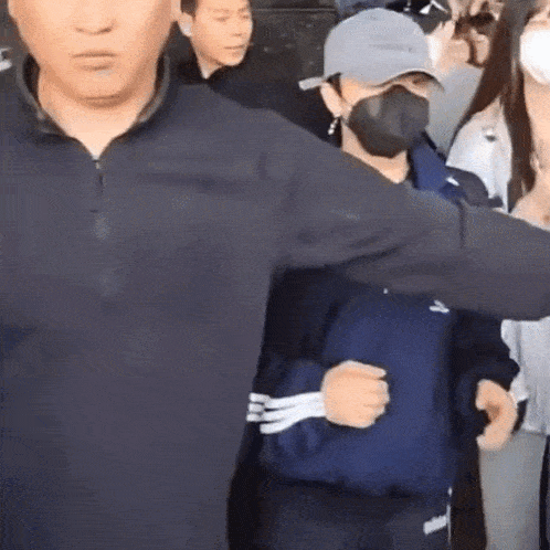 a man wearing a mask and a hat is being escorted by a man in a black jacket