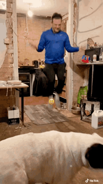 a man in a blue nike shirt is jumping in the air while a dog looks on