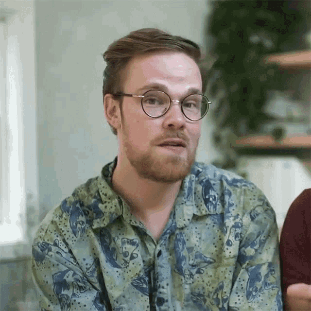 a man with glasses and a beard is wearing a shirt with a pattern
