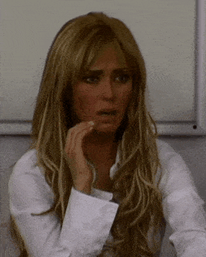 a woman with long blonde hair is wearing a white shirt and covering her mouth with her hand