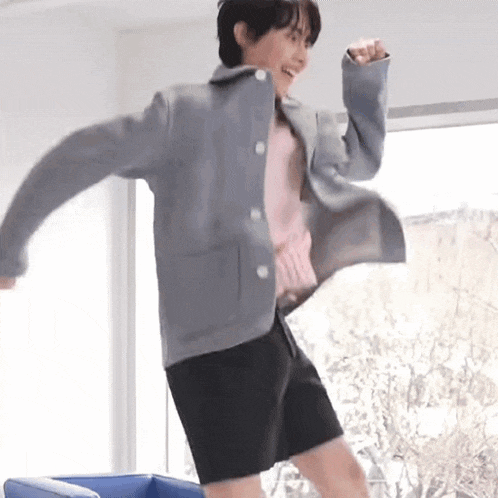 a young man in a gray jacket and black shorts is dancing in a room .