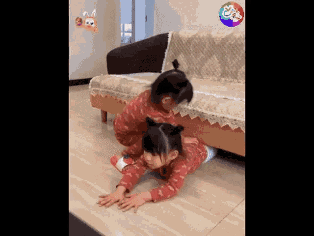 two little girls are crawling under a couch .