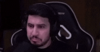 a man with a beard is sitting in a gaming chair and making an okay sign with his hand .