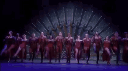 a group of dancers are dancing on a stage in front of a purple background .