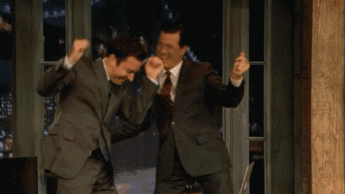 two men in suits and ties are dancing in front of a window