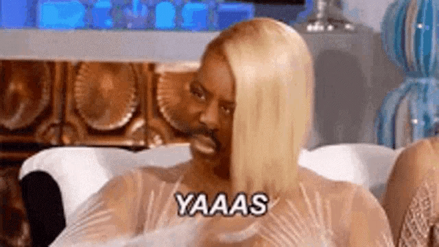 a woman with blonde hair and a mustache is sitting on a couch and making a funny face .