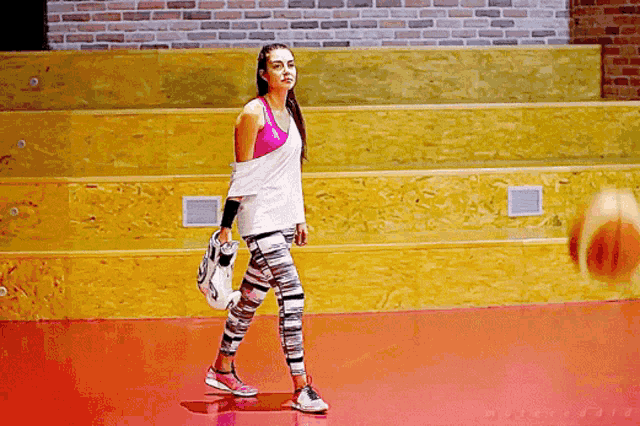 a woman is walking on a basketball court holding a basketball