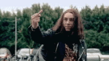 a man with long hair is giving the middle finger to the camera .