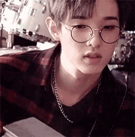 a young man wearing glasses and a plaid shirt is sitting in a restaurant .