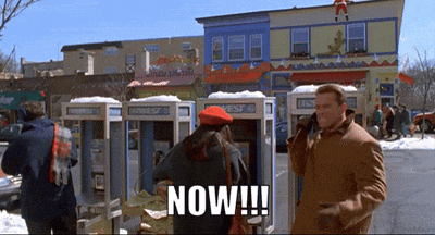 a man and woman are standing in front of a phone booth that says now !!!