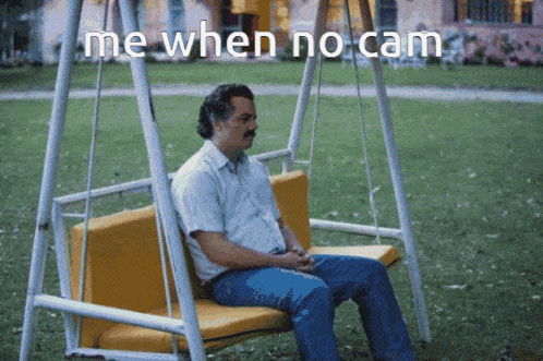a man is sitting on a swing with the words " me when no cam " written above him